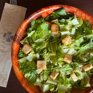 A Caesar salad in a wood bowl with a Colony Grill napkin.