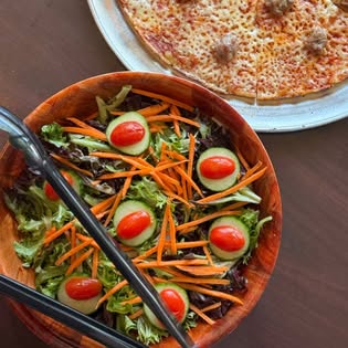 A garden salad with cucumber and tomato beside a cheese and sausage bar pie.