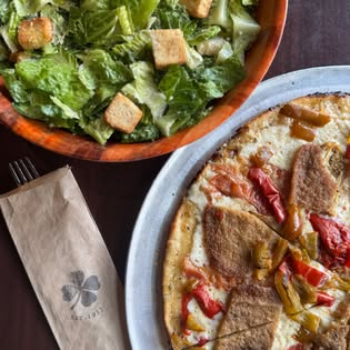 A pepper and sausage white pie with a Caesar salad and a Colony Grill napkin.