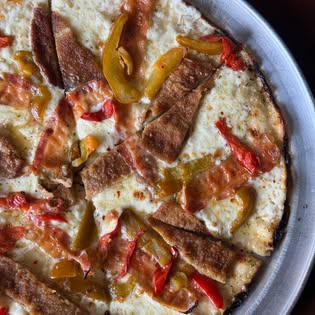 A close view of a bar pie with yellow and red peppers and sausage on a white base.