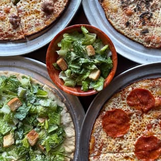 Several thin-crust bar pies and a Caesar salad bowl, seen from above on a wood table.