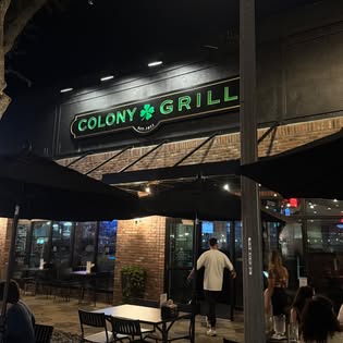 Colony Grill's lit green and gold sign above the patio tables on Central Avenue at night.